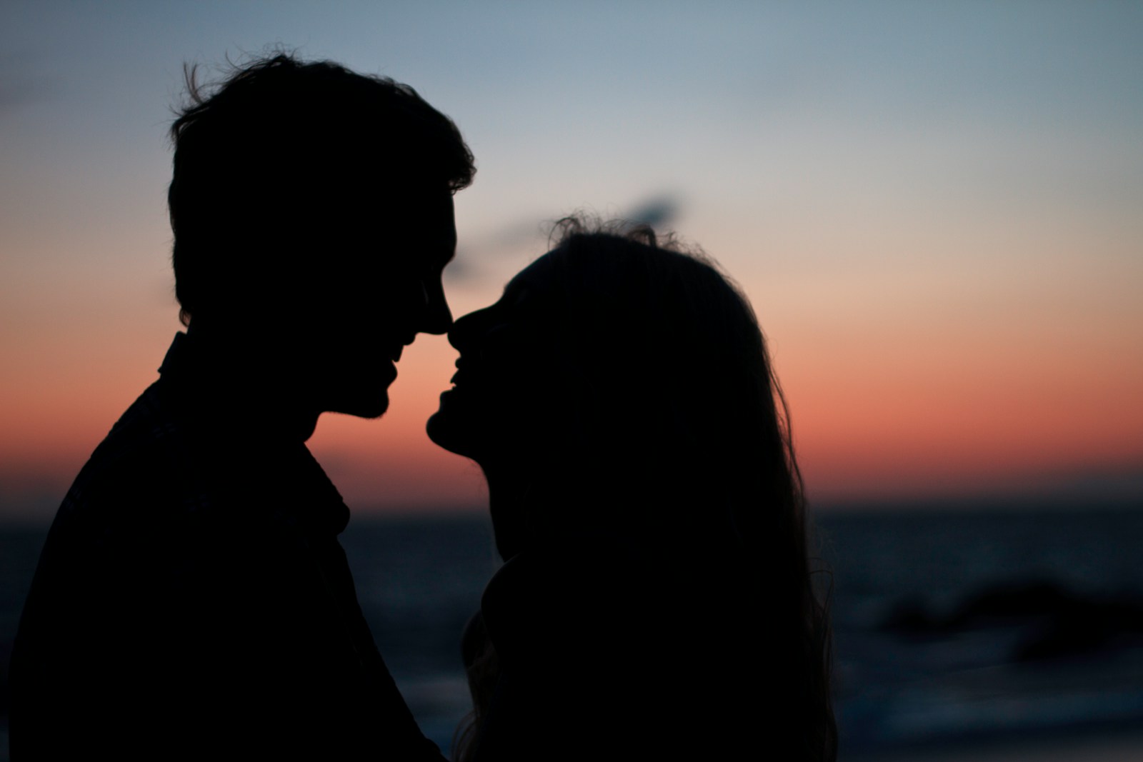 silhouette of man and woman about to kiss on beach during sunset